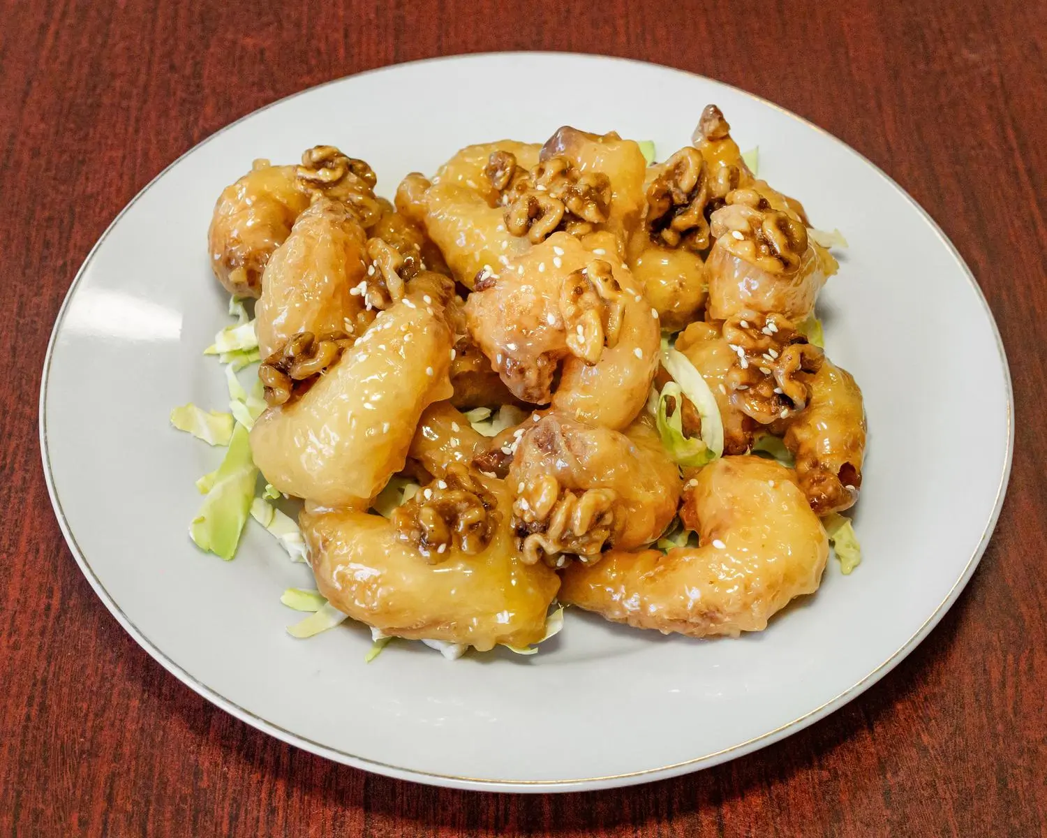 A plate of walnut prawns, featuring large prawns coated in a glossy sauce and topped with walnuts, served on a bed of shredded cabbage at Uncle Yu Restaurant，a Chinese Restaurant in Union City